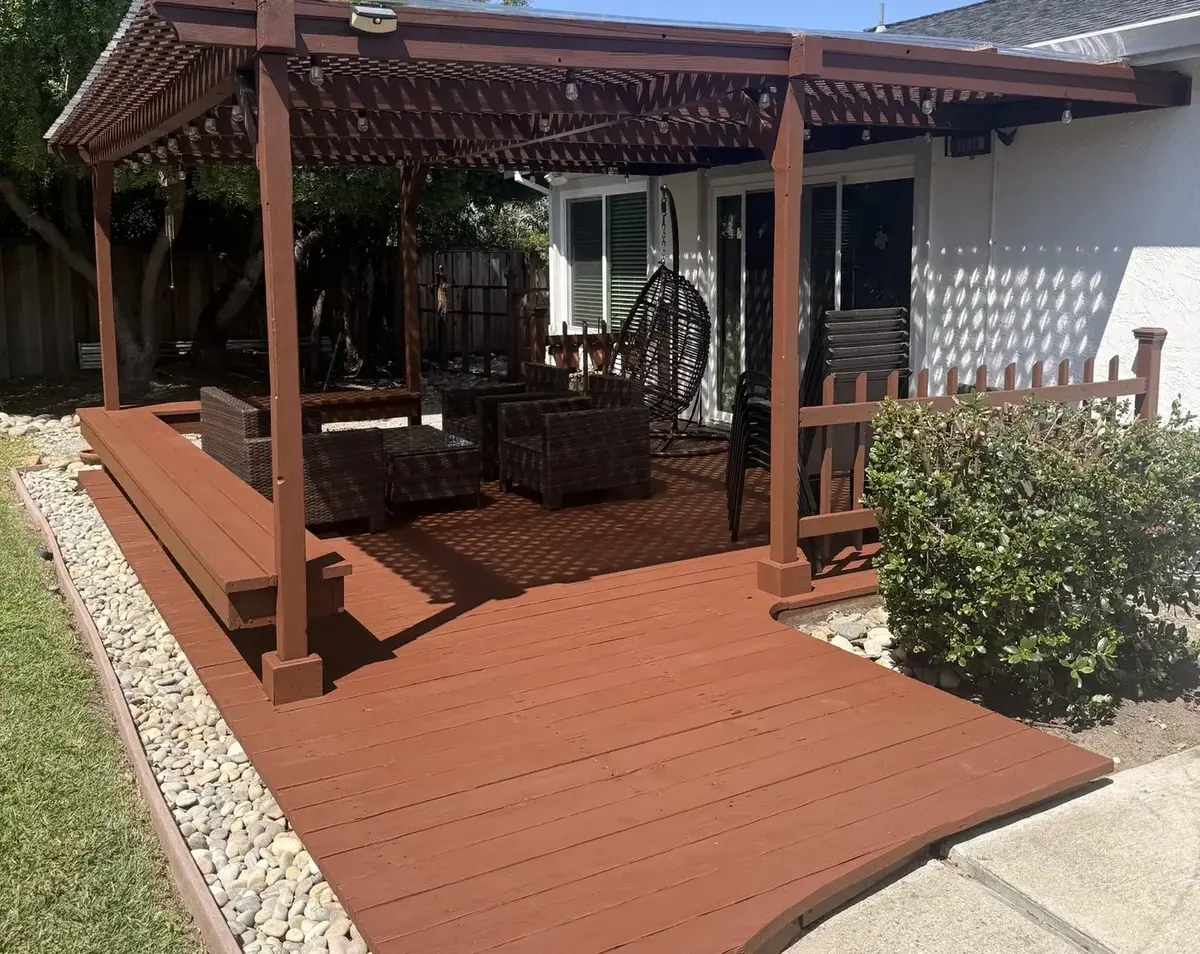 Stained timber pergola over a matching stained deck attached to a white house